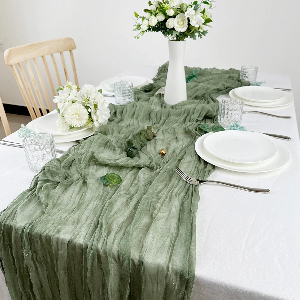 Table de baptême dressée en blanc avec un chemin de table en gaze de coton vert sauge