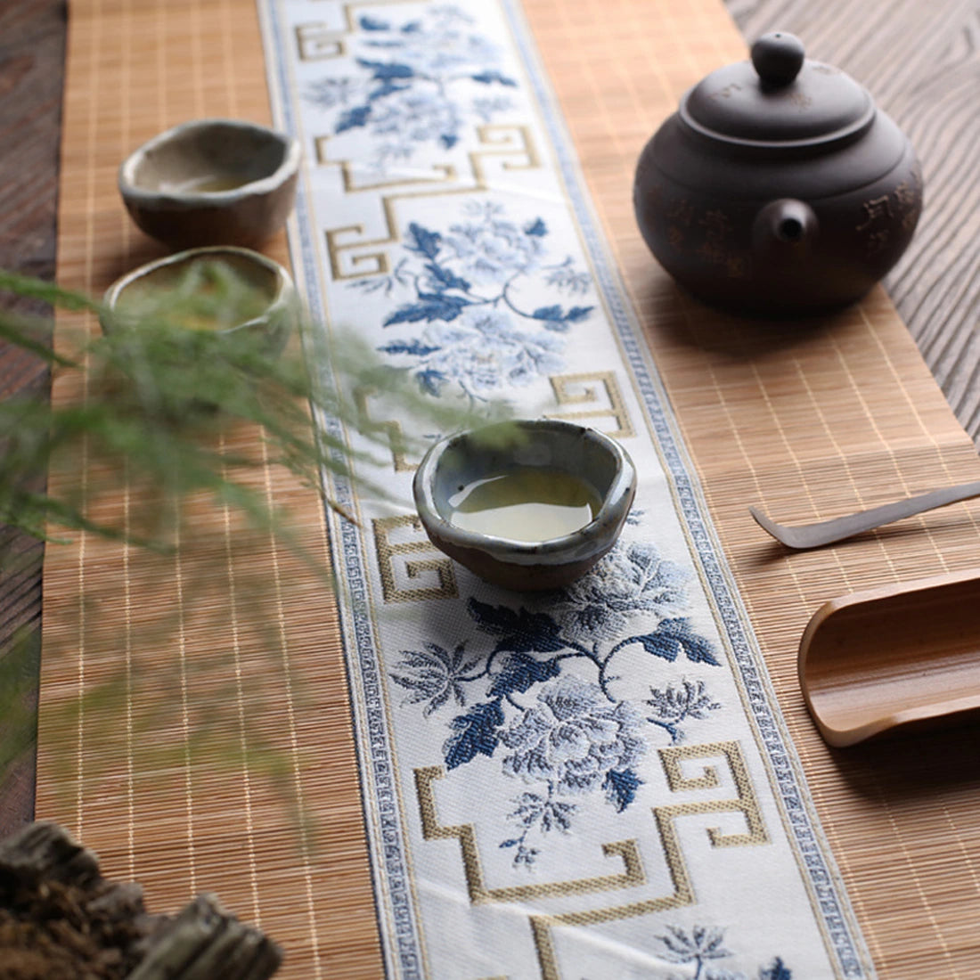 Chemin de table en bambou naturel dressé avec une théière, bandeau écru à fleurs bleues