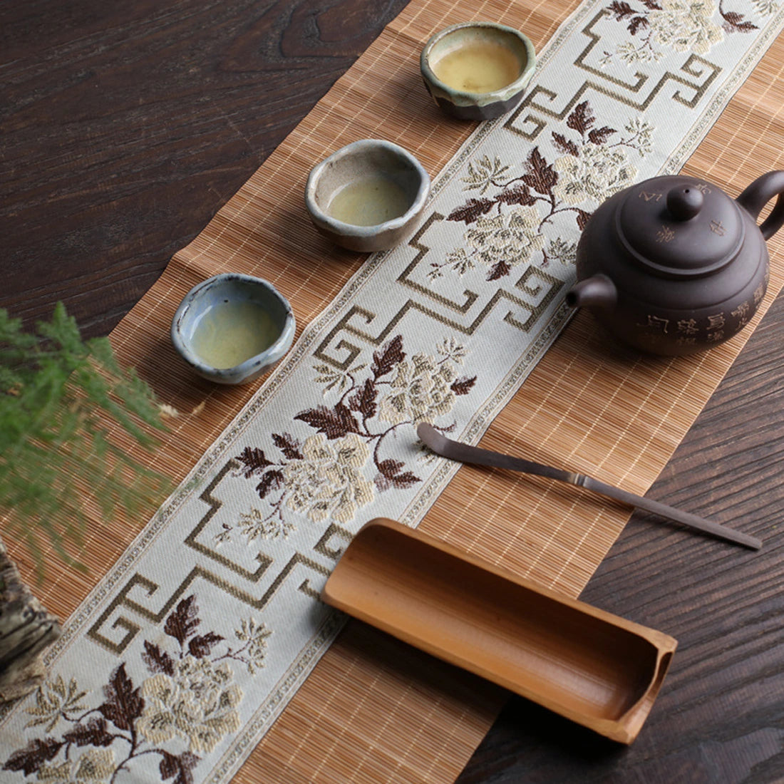 Chemin de table en bambou naturel dressé avec une théière et trois coupes, bandeau fleuri taupe