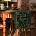 Chemin de table jacquard rinceaux verts et dorés à pompons dans un salon rétro